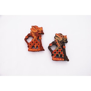 May include: Two flat, hand-painted wooden figures depicting the character Gatotkaca. Each figure features a dark brown base with intricate red and yellow patterns, including a checkered skirt design and the name GATOTKACA printed in yellow at the base.