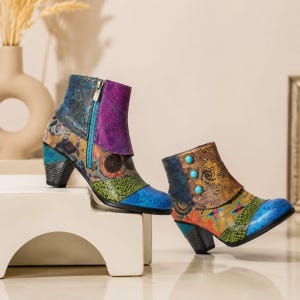 May include: A pair of ankle boots featuring a multi-colored patchwork design with floral and geometric patterns in shades of blue, purple, green, and yellow. One boot has a side zipper, while the other features three turquoise circular accents.