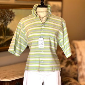 May include: A short-sleeved button-down shirt featuring horizontal stripes in shades of light green, white, and grey. The shirt has a ruffled collar, a front chest pocket, and a white tag attached to the center button with printed text.