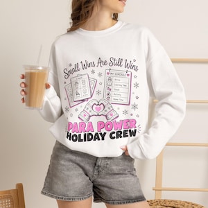 Peut inclure: Un sweat-shirt blanc à manches longues avec le texte Small Wins Are Still Wins et PARA POWER HOLIDAY CREW. Le motif comprend deux moufles formant un cœur, un emploi du temps visuel et des cartes de communication avec des flocons.