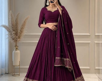 Peut inclure: Un ensemble lehenga violet profond composé d'un chemisier à manches trois-quarts avec un décolleté en cœur et d'une jupe longue plissée. La jupe et le dupatta assorti sont ornés d'une large bordure métallique dorée complexe.