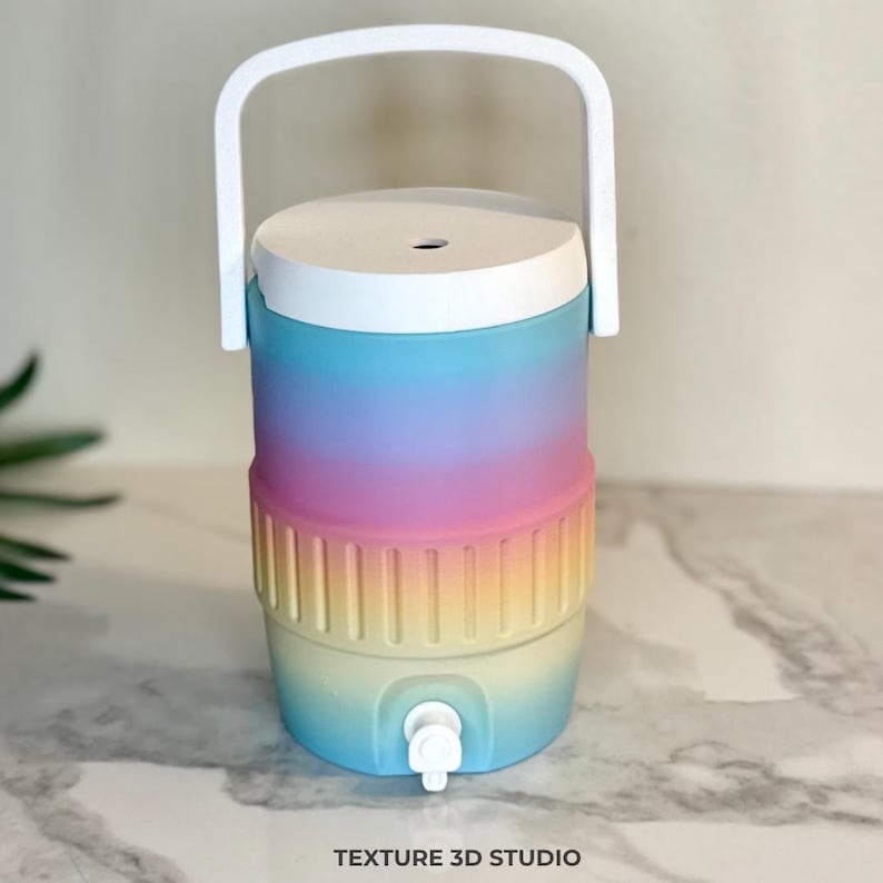 May include: A cylindrical beverage cooler featuring a pastel ombre gradient transitioning from blue to purple, pink, yellow, and light blue. It includes a white lid, a white top handle, and a white spigot at the base. The text TEXTURE 3D STUDIO is visible.