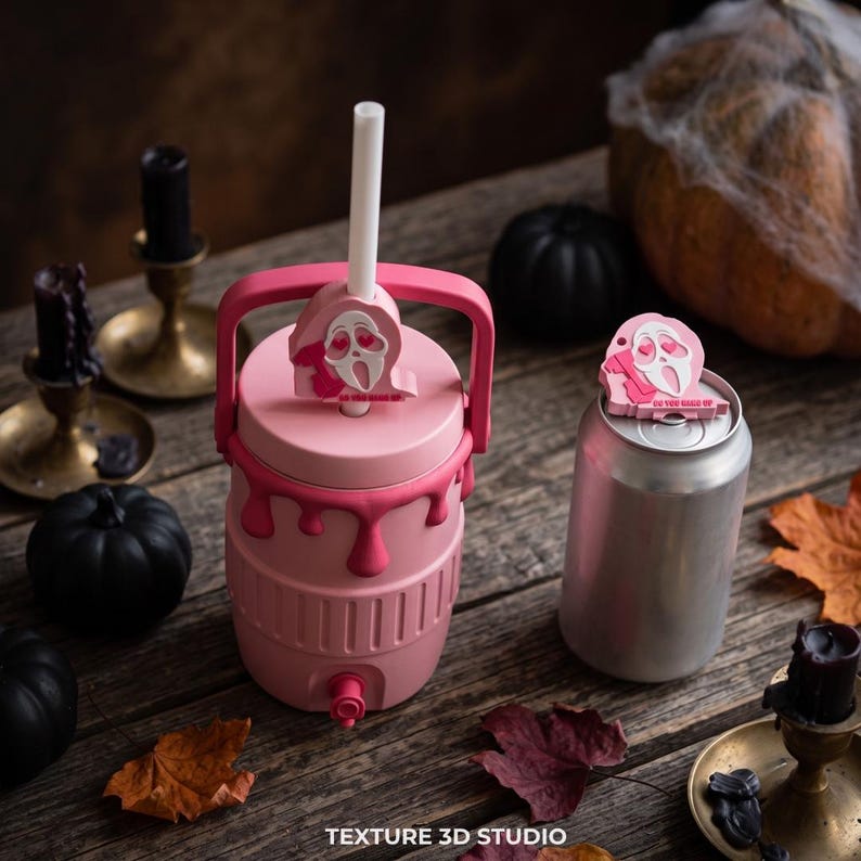 May include: A pink beverage cooler with a handle and a spigot, featuring a pink Ghostface topper with heart eyes and the text DO YOU LIKE SCARY MOVIES. Next to it is a silver aluminum can with a matching pink Ghostface topper on the lid.