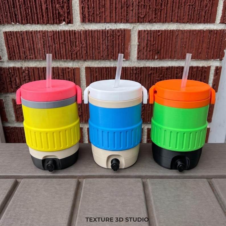 May include: Three cylindrical beverage coolers with spigots and straws. The first is pink, yellow, and black. The second is white, blue, and beige. The third is orange, green, and black. Each cooler features a ribbed midsection and a flat lid.