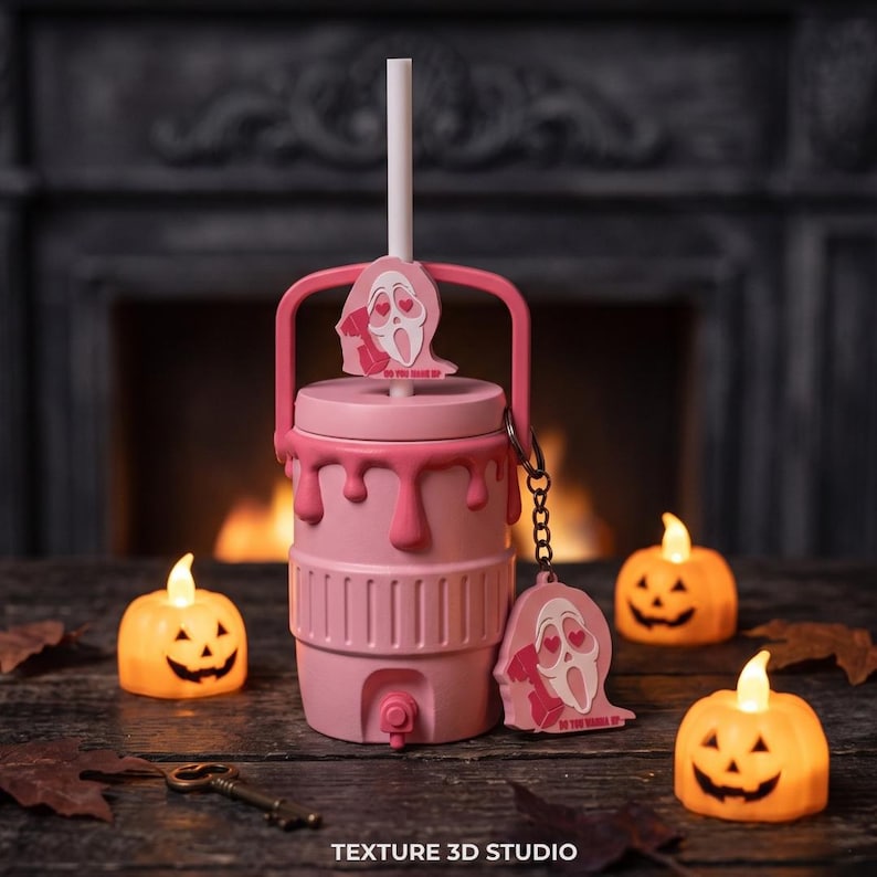 May include: A light pink beverage cooler with a handle and a spigot, featuring a white straw and a pink ghost-shaped charm with heart eyes and the text DO YOU LIKE SCARY MOVIES. Two orange jack-o'-lantern tea lights sit on either side.