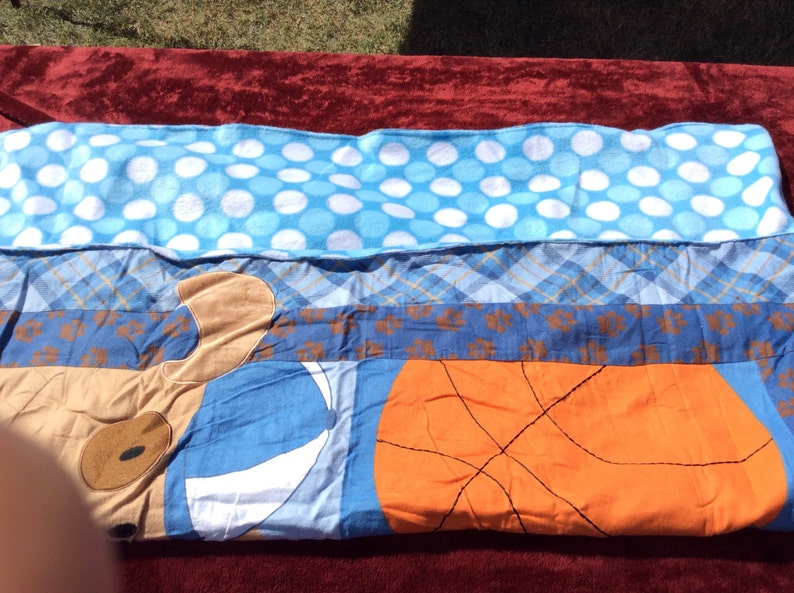 May include: A blue and brown patchwork quilt with a basketball, a dog, and white polka dots.