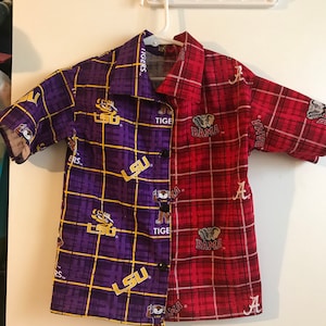 May include: A purple and red plaid button-up shirt with LSU and Alabama logos. The shirt is split down the middle, with LSU on the left and Alabama on the right.