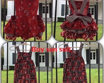 May include: Two baby outfits, one red and white with ruffles and the other red and black with a checkered pattern. Both outfits have the letters "A" and "Crimson Tide" printed on them.