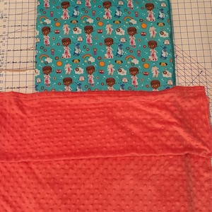 May include: A turquoise and white patterned toddler bed with a red blanket. The pattern features a cartoon doctor character.