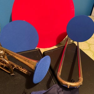 May include: A red, blue, and gold musical instrument set with a trombone, trumpet, and three blue practice mutes. A black case with the word "KING" on it is visible in the background.