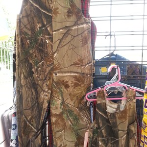 May include: Two sleeveless camouflage-patterned shirts hanging on a rack. The shirts are made of a soft, lightweight fabric and have a relaxed fit. The shirts are perfect for casual wear.