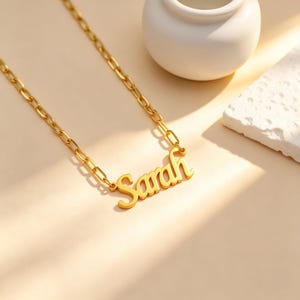 May include: A gold-toned necklace featuring a nameplate pendant with the name Sarah in a cursive script font. The pendant is attached to a thick, elongated oval link chain, creating a bold and structured look for this personalized jewelry piece.