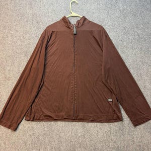 May include: A solid brown long-sleeve zip-up jacket with a mock neck collar. The garment features a full-length front zipper, long sleeves, and a small rectangular brand label on the lower left side. The fabric has a smooth, lightweight appearance.