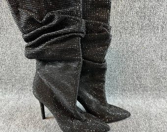 May include: A pair of black mid-calf boots featuring a pointed toe and a stiletto heel. The entire exterior surface of the boots is covered in small, reflective black rhinestones, creating a textured appearance with a slouchy, gathered shaft.