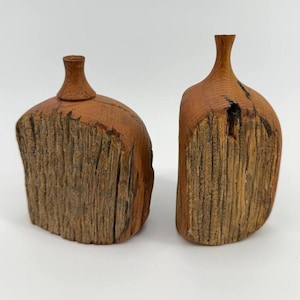 Op de afbeelding: Twee decoratieve houten sculpturen in de vorm van flessen met smalle halzen. Elk stuk heeft een ruw, getextureerd vooroppervlak met zichtbare houtnerf en natuurlijke scheuren, in contrast met een gladde, afgeronde bovenkant en hals.