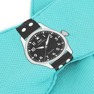 Peut inclure: Un accessoire en tissu texturé turquoise vif arborant une impression graphique d'une montre automatique IWC Schaffhausen noire et blanche. Le cadran affiche des chiffres, des aiguilles et le nom de la marque en blanc sur un bracelet noir à pois.