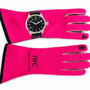 Pode incluir: Um par de luvas de corrida rosa brilhante com acabamento preto e marca OMP. Uma luva apresenta um relógio de pulso IWC Schaffhausen preto com pulseira de couro preta e números brancos. A outra luva exibe o texto IWC SCHAFFHAUSEN em preto.