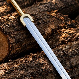 Può includere: Una spada a doppio taglio con una lama in acciaio lucido color argento e un'impugnatura color oro metallizzato. L'elsa presenta una caratteristica guardia a forma di U che collega la lama all'impugnatura cilindrica, terminante in un pomolo piatto.