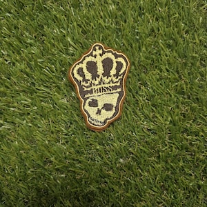 May include: An embroidered patch featuring a dark brown skull topped with a golden yellow crown. The word BOSS is stitched in golden yellow thread across the center of the design, positioned between the crown and the skull's eye sockets.