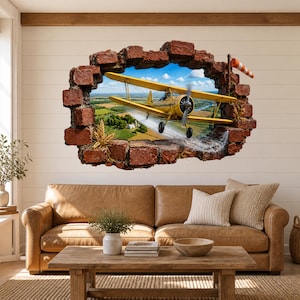 May include: A wall decal featuring a 3D-style hole in a red brick wall, revealing a yellow biplane flying over a green landscape. The plane is spraying a mist over fields, with a small orange and white windsock attached to the brick frame.