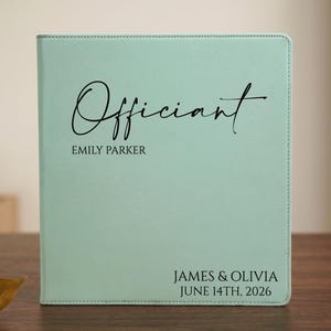 May include: A mint green binder featuring the word Officiant in a black script font, with the name EMILY PARKER printed below. The bottom right corner displays the text JAMES & OLIVIA and the date JUNE 14TH, 2026 in a clean black sans-serif font.