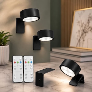 May include: Three matte black cylindrical wall-mounted LED lights with four circular light apertures each. Two lights are mounted vertically, and one is angled on a surface. Two white remote controls with buttons for color and timer settings.