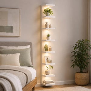 May include: A tall, vertical white wall-mounted shelving unit featuring eight individual shelves. Each shelf is illuminated by integrated warm LED lighting, displaying various decorative items including small potted plants, vases, and a picture frame.