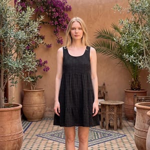 Puede incluir: Un vestido sin mangas hasta la rodilla con un patrón de cuadros en verde oscuro y negro. La prenda tiene un cuello redondo y un diseño de falda escalonada con costuras horizontales que crean una silueta sutilmente fruncida en la parte inferior.