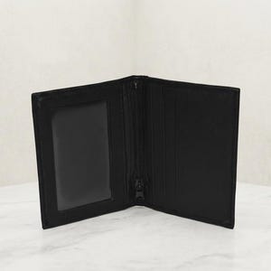 May include: A black bi-fold wallet featuring a clear plastic ID window on the left side and multiple vertical card slots on the right side. The center of the wallet includes a vertical zipper closure, providing a secure compartment for small items.