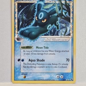 May include: A trading card featuring the character Umbreon with 160 HP, labelled as a Delta Species. The card displays a blue water-themed background with seaweed, text detailing the Moon Tide ability and Aqua Shade attack, and the text 2026-UNOFFICIAL/CUSTOM CARD at the bottom.