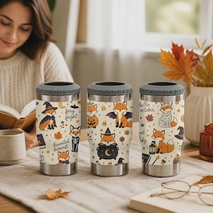 Peut inclure: Trois gobelets en acier inoxydable avec un revêtement crème illustré de renards orange en costumes d'Halloween, incluant sorcière, momie et squelette, avec des citrouilles, chauves-souris, étoiles et le texte foxy fright et hello october.