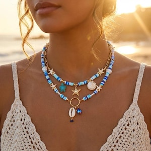 May include: A layered necklace set featuring blue and white heishi beads, gold-tone chain links, and charms including a turquoise sea turtle, gold starfish, white seashell, and a small blue teardrop bead, all arranged on a gold-tone metal base.