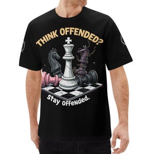 Op de afbeelding: Een zwart t-shirt met een afbeelding van een witte koning schaakstuk op een schaakbord, omringd door omgevallen zwarte en roze schaakstukken. De tekst "THINK OFFENDED?" staat in beige erboven en "Stay Offended." in het wit eronder.