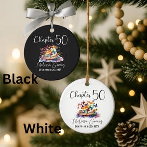 Peut inclure: Deux ornements ronds en céramique, un noir et un blanc, chacun avec un ruban argenté. Le texte indique Chapter 50, Melissa Gomez et December 20, 1975, au-dessus d'une illustration colorée d'un livre ouvert avec des papillons sortant des pages.