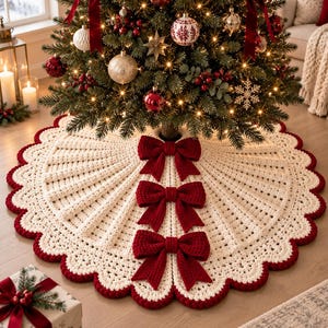 May include: A circular cream-colored crocheted Christmas tree skirt featuring a scalloped edge trimmed in deep red. The skirt is adorned with three large, textured dark red bows aligned vertically along the front opening of the fabric.