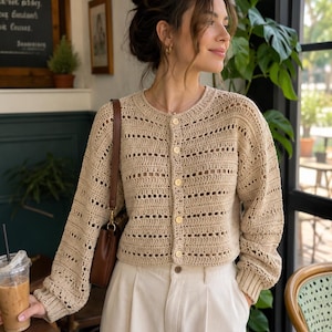 May include: A beige long-sleeved crochet cardigan featuring a round neckline, a button-down front with five light-colored buttons, and a repeating pattern of solid stitches alternating with horizontal rows of openwork, finished with ribbed cuffs.