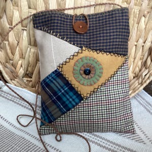 May include: A rectangular crossbody bag constructed from various fabric patches including navy blue gingham, beige twill, blue plaid, and a tan felt diamond shape. It features a brown button closure, a thin brown cord strap, and decorative stitching.