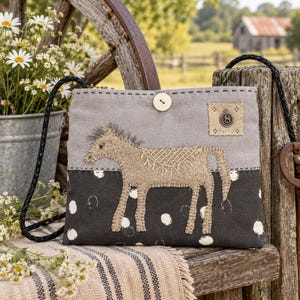 May include: A rectangular crossbody bag featuring a light gray upper section and a dark gray lower section with white polka dots. An embroidered tan horse with a saddle design is centered on the front. It has a single light button closure and a black braided strap.