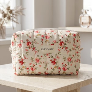 May include: A rectangular quilted cosmetic bag in an off-white fabric featuring a repeating floral pattern of red and pink roses with green leaves. The bag has a centered rectangular fabric label with the text PURSEMARK printed in black.