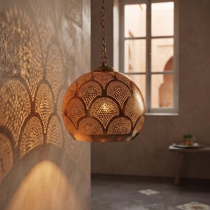 Peut inclure: Une suspension sphérique en laiton dotée d'un motif festonné perforé qui projette des ombres lumineuses complexes. Le dôme en métal est suspendu par une chaîne en laiton assortie, présentant une finition métallique chaude et des découpes.