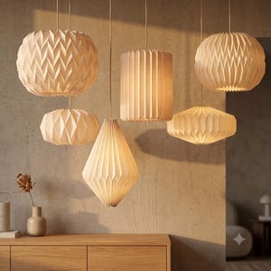 May include: A collection of six off-white pendant lights with various geometric pleated paper shades. The fixtures include spherical, cylindrical, and diamond-shaped designs, all suspended by thin cords, emitting a warm glow in a room.