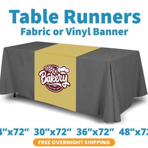 May include: A rectangular table runner in a solid gold color featuring a circular maroon logo with a wheat stalk and chef hat icon, centered on a dark gray tablecloth. The text Bakery Bread and Cakes is printed on the logo.