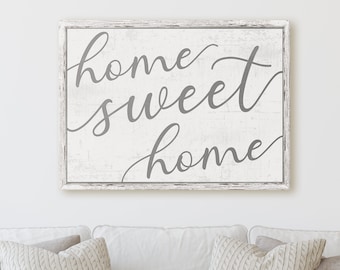 May include: A white framed sign with a distressed wood background. The sign features the text "home sweet home" in a gray cursive font.
