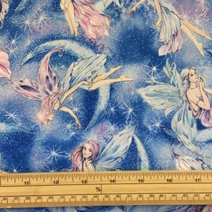 May include: A blue fabric with a repeating pattern of fairies flying among stars and crescent moons. The fabric is measured with a ruler in inches.