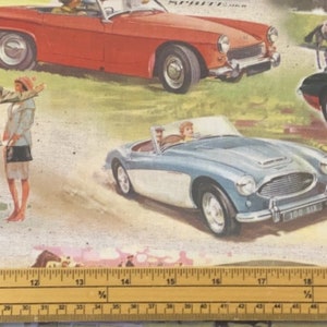 May include: A vintage illustration of a red and white sports car, a blue and white sports car, and a black and red sports car. The cars are on a green grassy field with a wooden ruler in the foreground. The ruler is marked with inches and fractions of an inch.