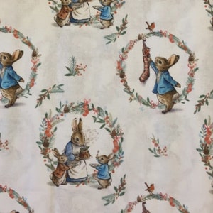 May include: White fabric with a repeating pattern of Peter Rabbit and friends in a Christmas wreath. The fabric features a blue and brown Peter Rabbit holding a plate of food, a smaller brown rabbit holding a plate, and a smaller blue rabbit holding a plate. The fabric also features a blue and brown Peter Rabbit holding a stocking.