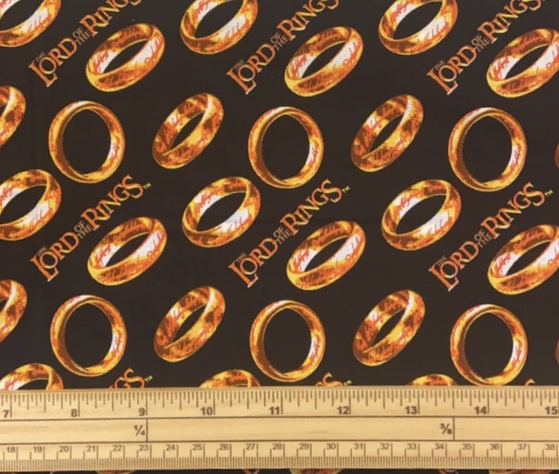 May include: Black fabric with a repeating pattern of gold rings and the words "The Lord of the Rings" in white.