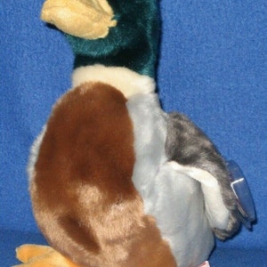 May include: A plush toy duck with brown, gray, and blue feathers. The duck has a green head and a yellow beak. The toy is sitting on a blue surface.