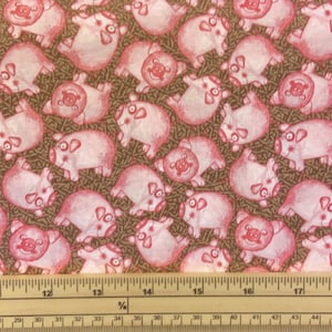 May include: A brown fabric with a repeating pattern of pink pigs. The fabric is measured with a ruler that shows 17 inches.