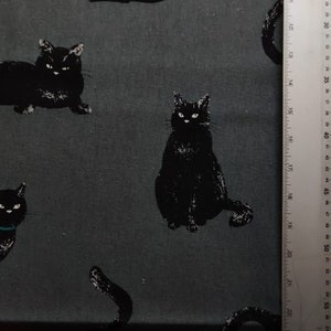 以下が含まれることがあります： 黒と白の生地に、黒い猫の繰り返し模様が描かれています。生地は濃いグレーです。
